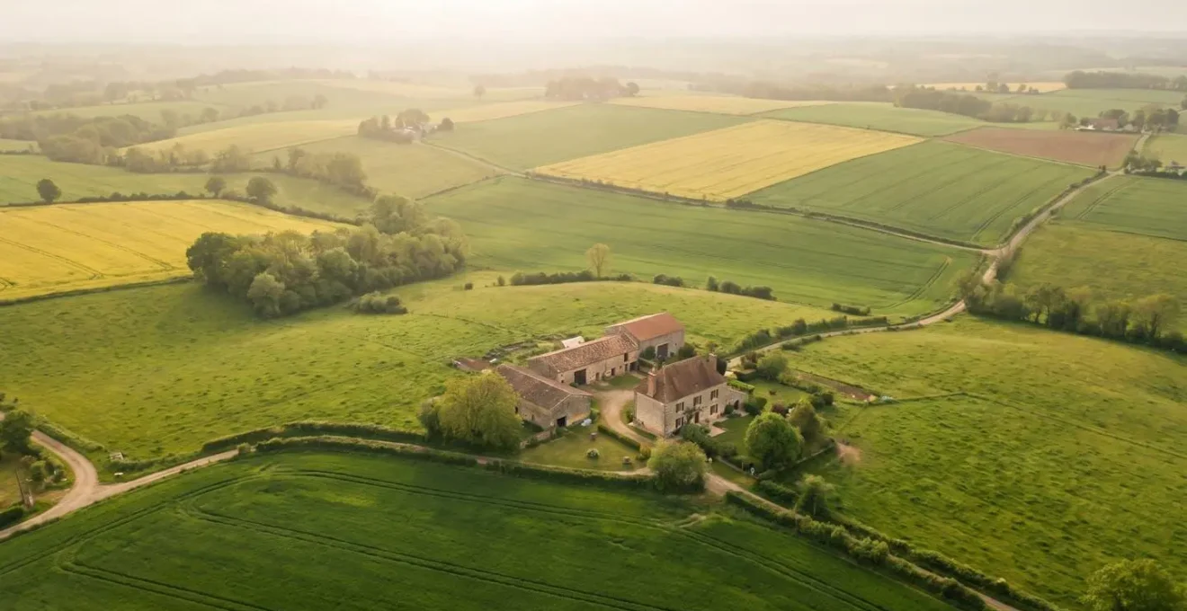 Vue aérienne de champs agricoles français au printemps avec une ferme visible au centre, évoquant la transition énergétique des territoires ruraux